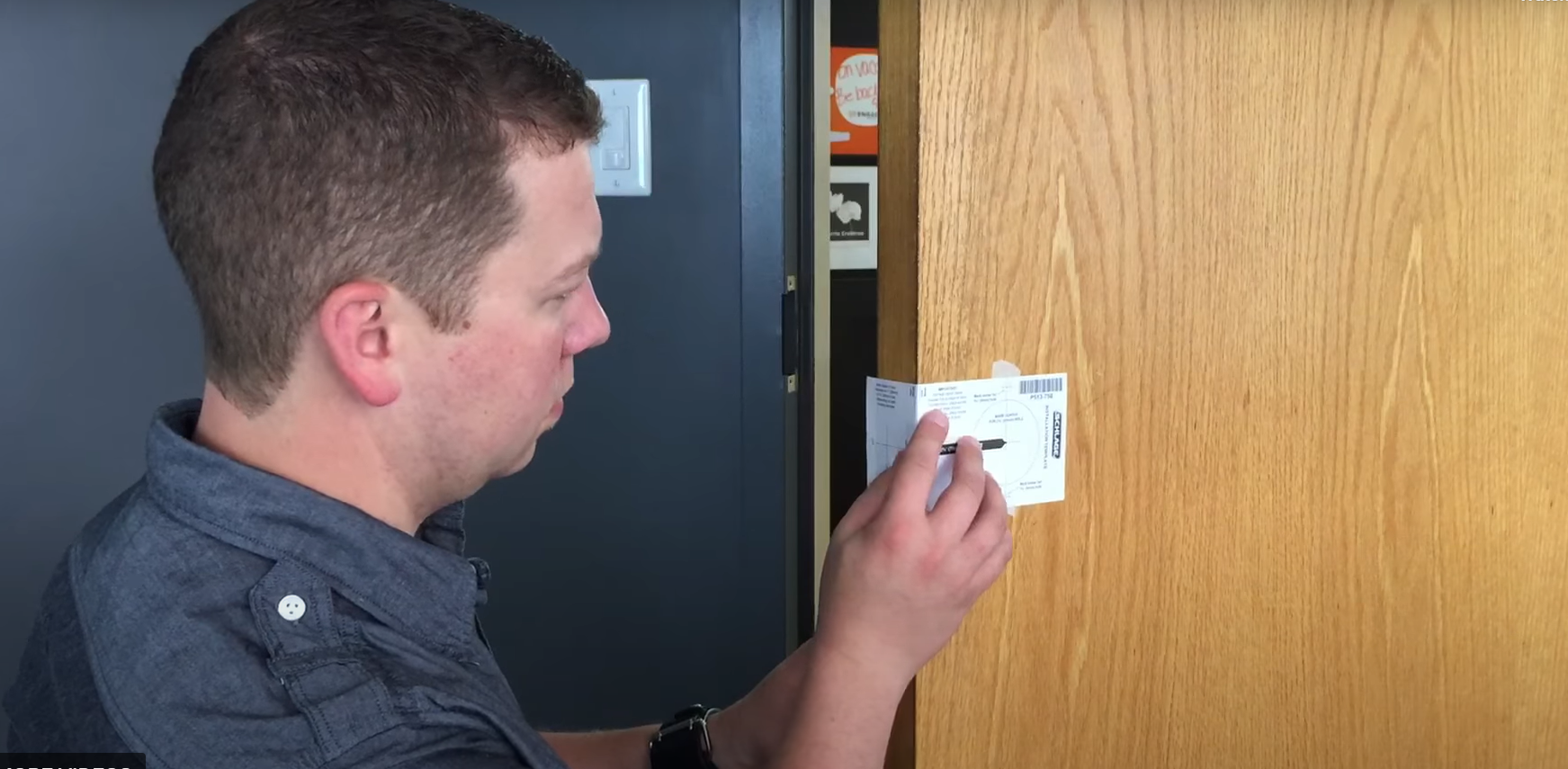 A man is seen from the side, focusing on installing or inspecting an electronic access control keypad next to a wooden door.